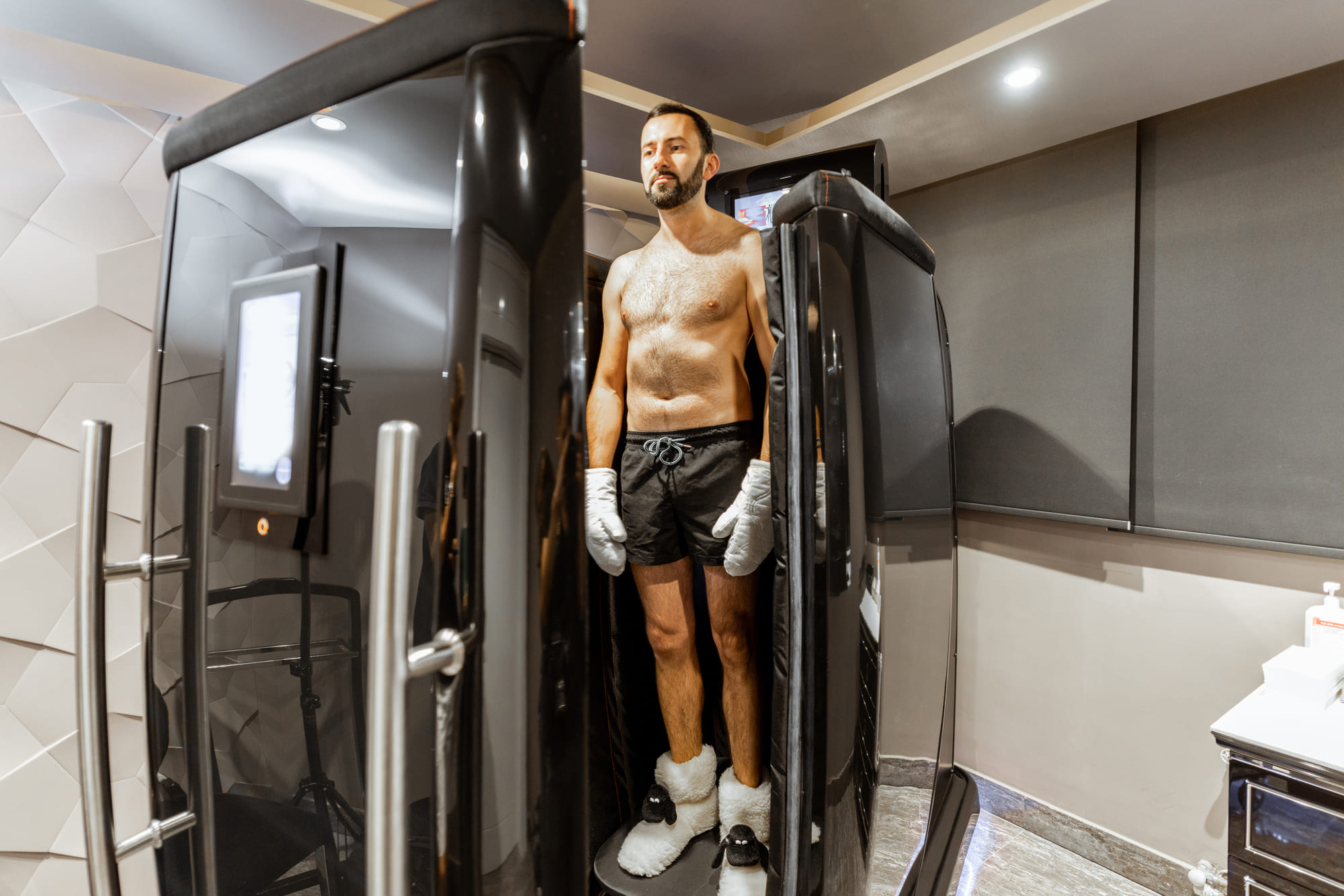 A smiling athlete stands confidently before a hyperbaric oxygen therapy chamber, representing the positive impact of HBOT for athletes on recovery and performance enhancement.